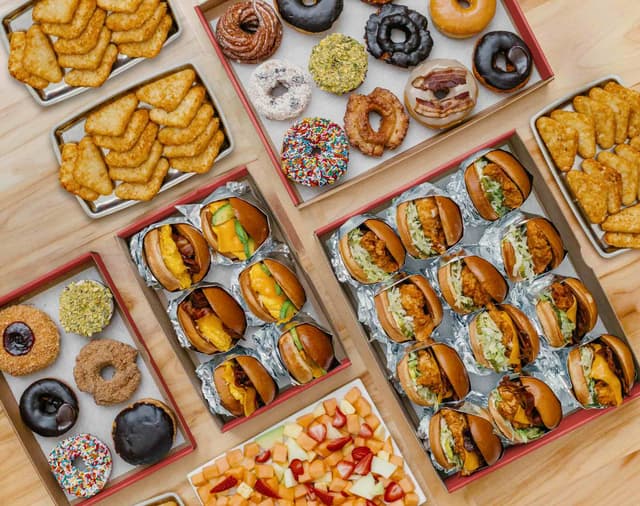 Spread of catering offerings including sandwiches, donuts, fruit and hash browns.