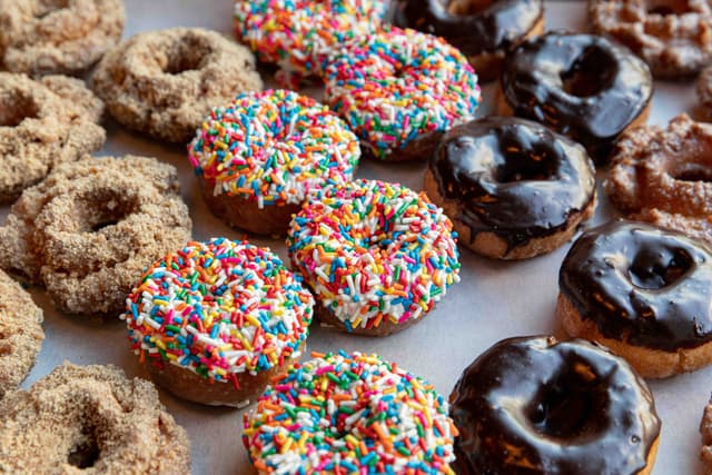 Spread of Cinnamon Crunch, Sprinkle, Chocolate and Old Fashioned Donuts on a tray.