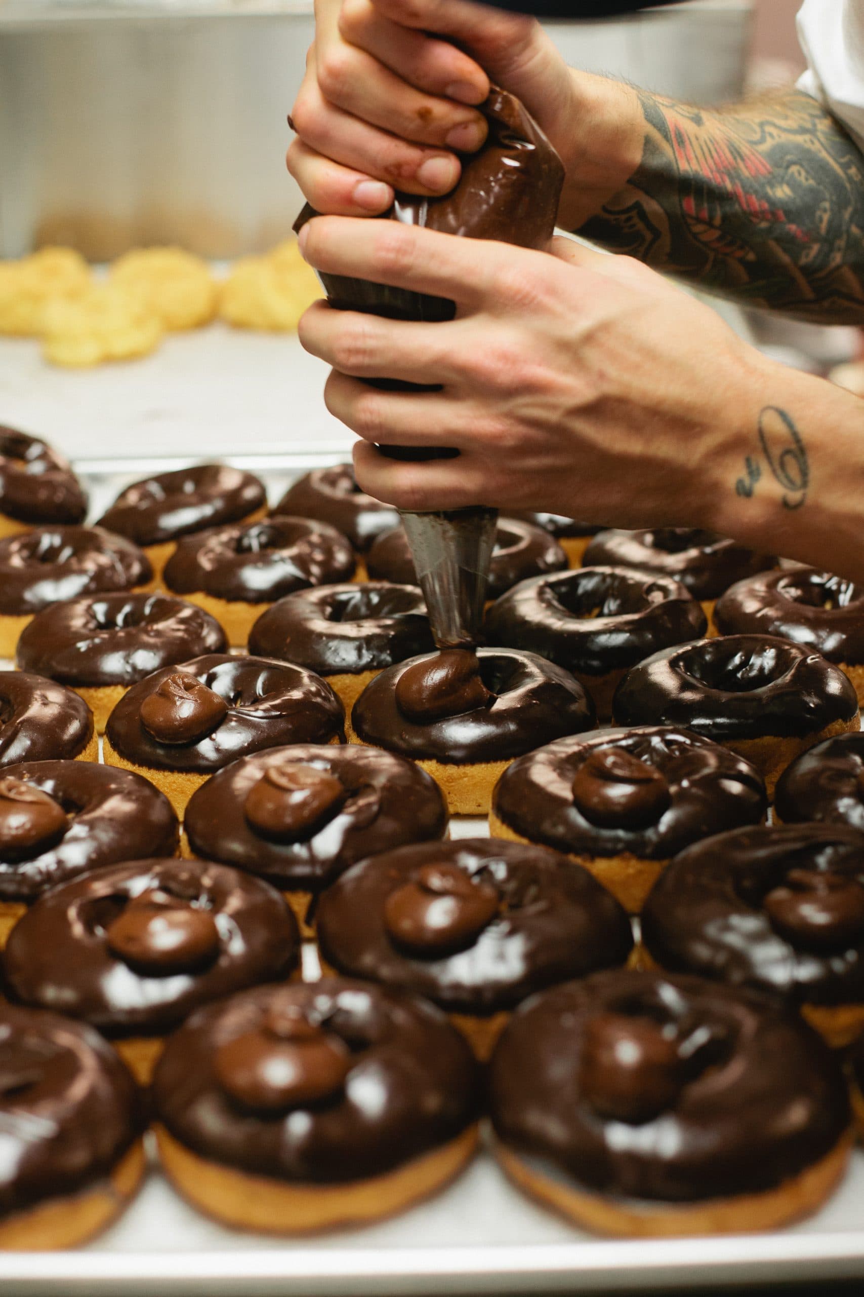 Chef piping chocolate onto donuts.